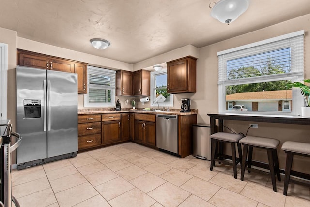 kitchen featuring light tile patterned floors, stainless steel appliances, light stone counters, and sink