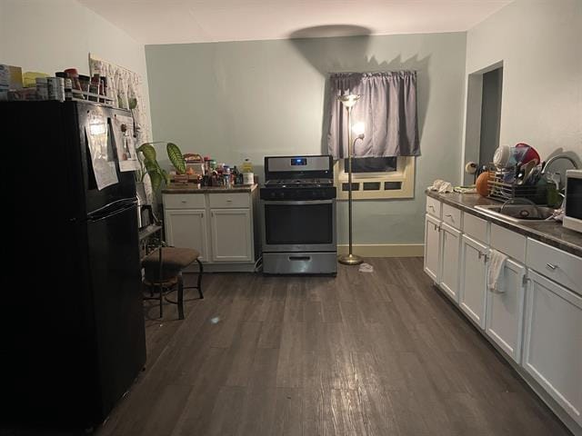 kitchen featuring dark hardwood / wood-style flooring, black fridge, sink, stainless steel range oven, and white cabinetry