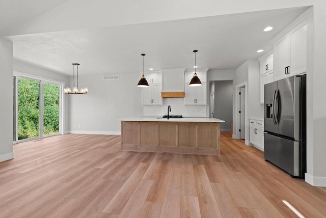 kitchen with a center island with sink, stainless steel fridge, white cabinetry, and hanging light fixtures