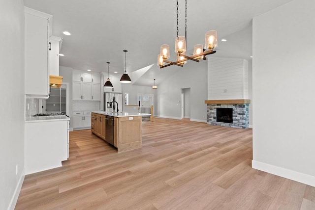 kitchen featuring appliances with stainless steel finishes, backsplash, decorative light fixtures, white cabinets, and an island with sink