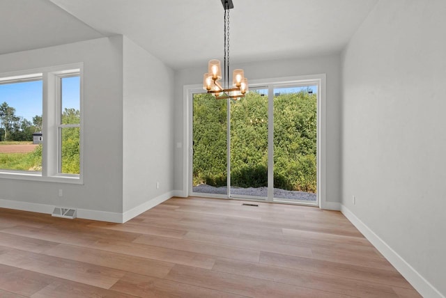 unfurnished dining area with light wood-type flooring, an inviting chandelier, and a healthy amount of sunlight