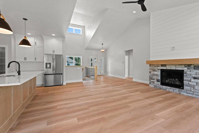 unfurnished living room with ceiling fan, sink, light hardwood / wood-style flooring, a fireplace, and a high ceiling