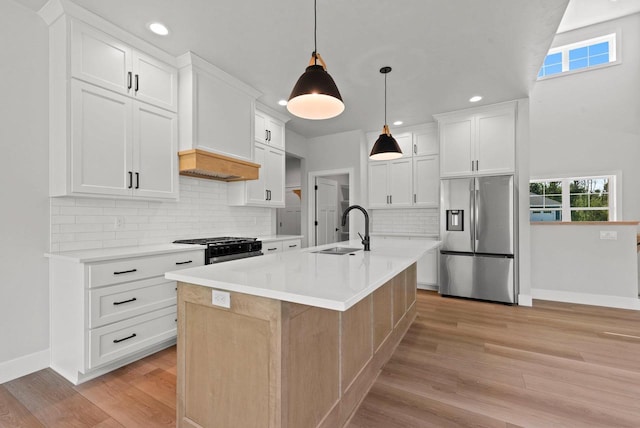 kitchen with a kitchen island with sink, white cabinets, hanging light fixtures, sink, and stainless steel appliances