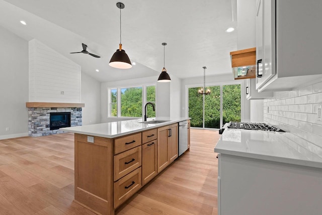 kitchen with pendant lighting, a kitchen island with sink, stainless steel dishwasher, a fireplace, and light stone counters