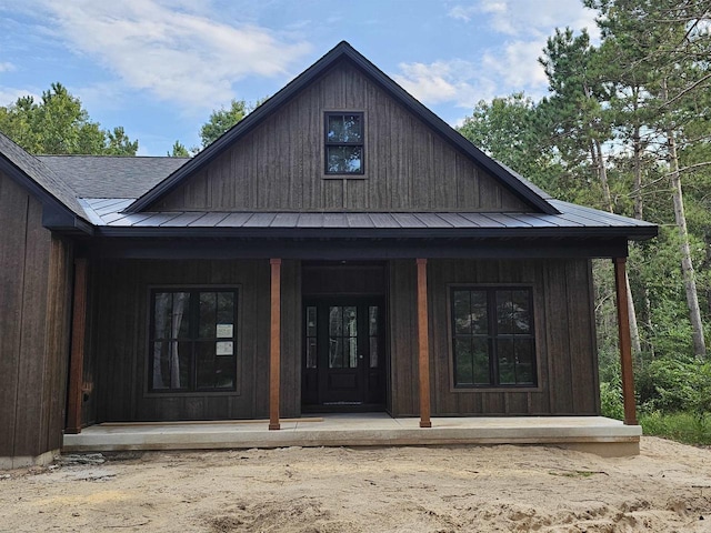 entrance to property featuring covered porch, metal roof, a standing seam roof, and roof with shingles