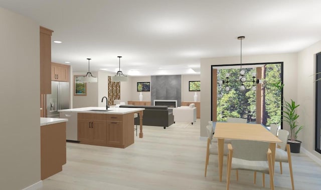 kitchen featuring an island with sink, a sink, stainless steel fridge, light wood finished floors, and light countertops