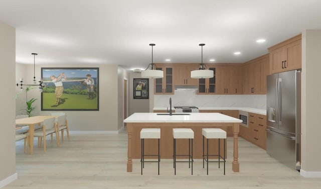 kitchen featuring glass insert cabinets, a center island with sink, light countertops, stainless steel fridge, and a sink