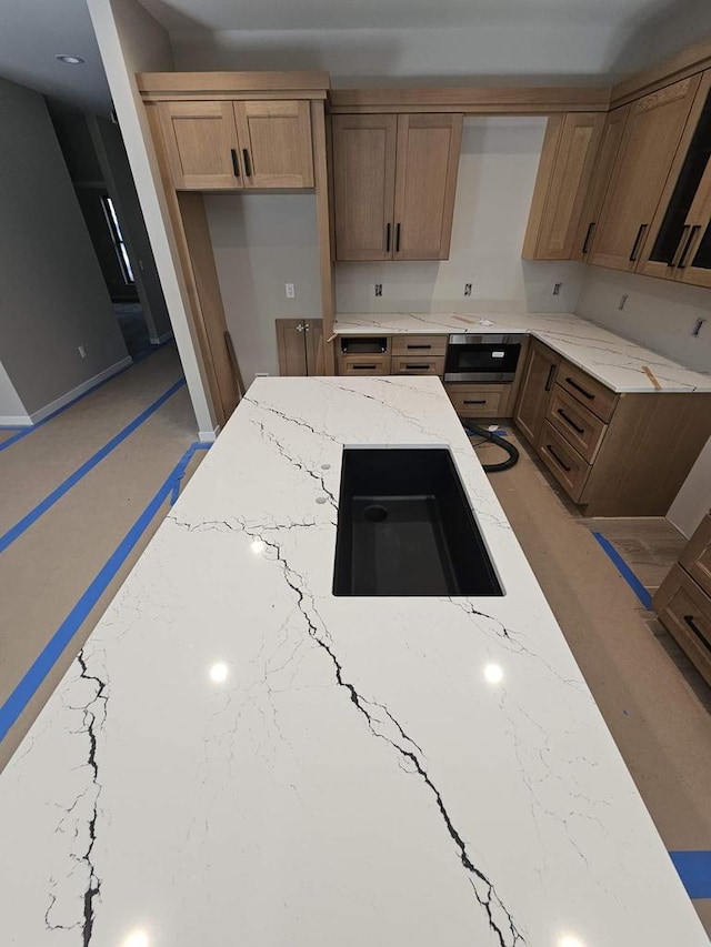 kitchen with stainless steel microwave, light stone countertops, and a sink