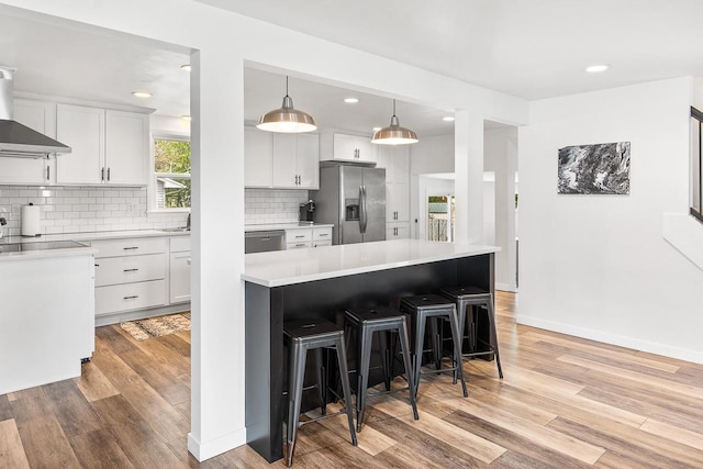 kitchen featuring stainless steel appliances, white cabinetry, hanging light fixtures, and a kitchen island