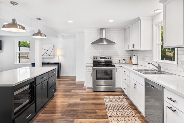 kitchen with appliances with stainless steel finishes, sink, wall chimney range hood, pendant lighting, and white cabinetry