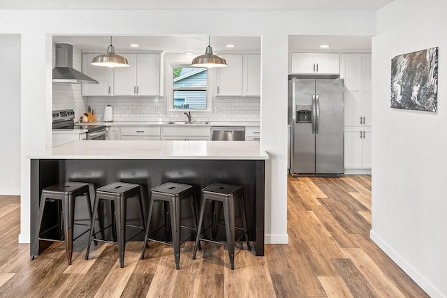 kitchen with white cabinets, wall chimney range hood, decorative backsplash, decorative light fixtures, and stainless steel appliances