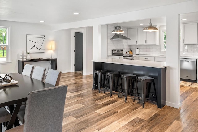 kitchen with a kitchen bar, backsplash, stainless steel appliances, pendant lighting, and white cabinets