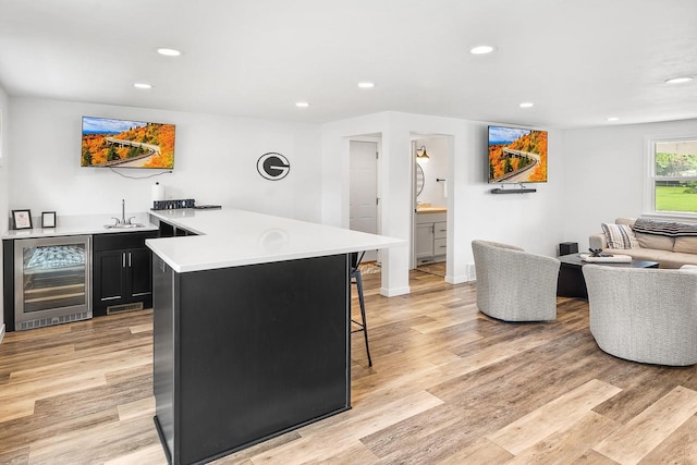 kitchen featuring a kitchen bar, light hardwood / wood-style floors, beverage cooler, and sink