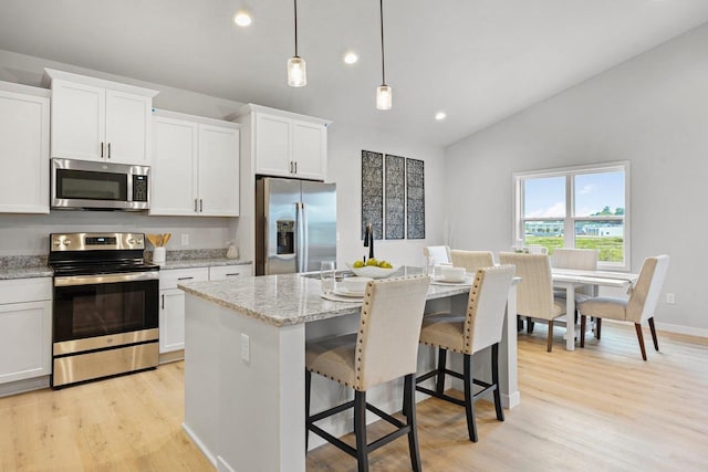 kitchen featuring pendant lighting, lofted ceiling, a kitchen island with sink, white cabinetry, and stainless steel appliances