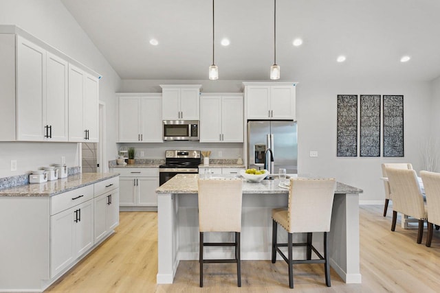 kitchen featuring white cabinets, light stone countertops, an island with sink, decorative light fixtures, and stainless steel appliances