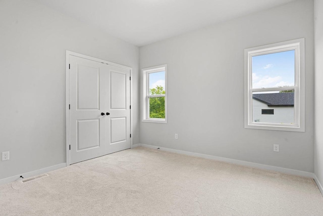 unfurnished bedroom featuring a closet, light carpet, and multiple windows