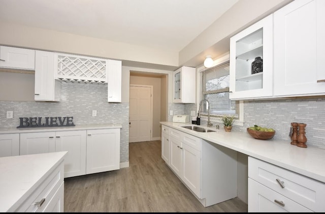 kitchen with decorative backsplash, white cabinetry, sink, and light wood-type flooring