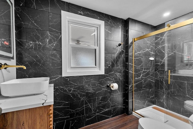 bathroom featuring a shower with door, vanity, tile walls, and toilet