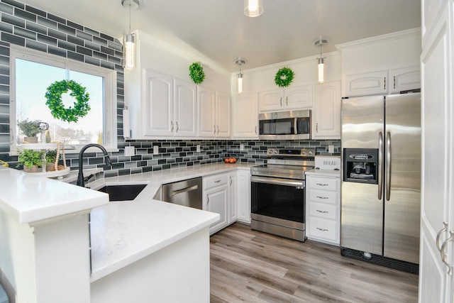 kitchen with sink, kitchen peninsula, decorative light fixtures, white cabinetry, and stainless steel appliances