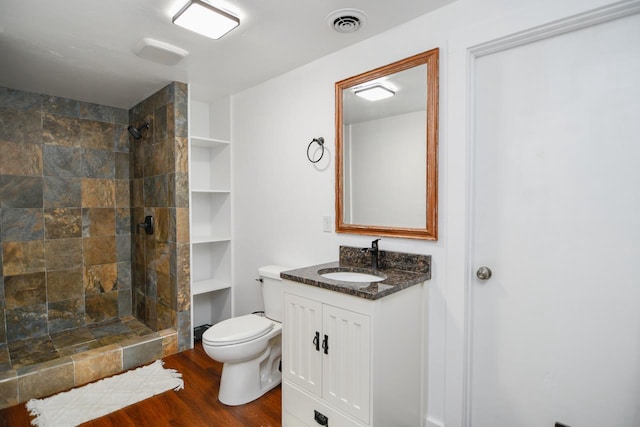 bathroom featuring a tile shower, hardwood / wood-style flooring, vanity, and toilet