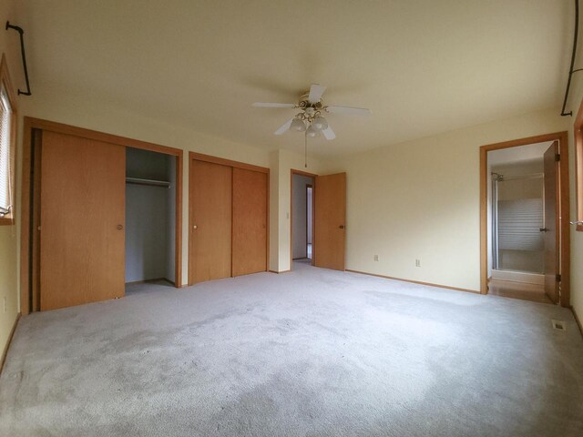 unfurnished bedroom with light colored carpet, ceiling fan, and multiple closets