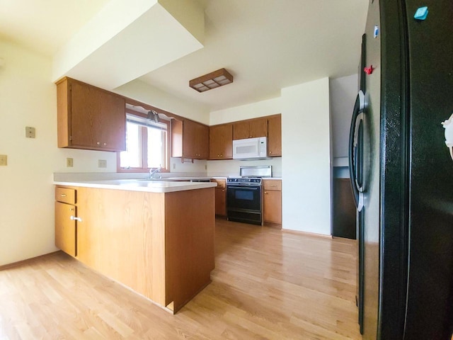 kitchen featuring black appliances, kitchen peninsula, sink, and light hardwood / wood-style flooring