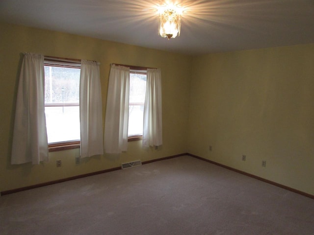 empty room featuring carpet, a healthy amount of sunlight, and a chandelier