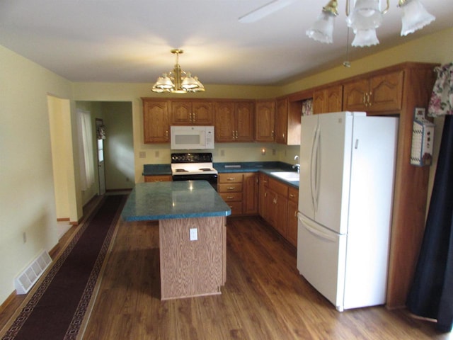 kitchen with dark hardwood / wood-style flooring, white appliances, sink, an inviting chandelier, and a kitchen island