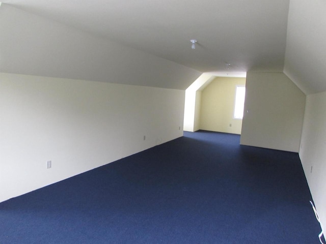 additional living space with dark colored carpet and vaulted ceiling