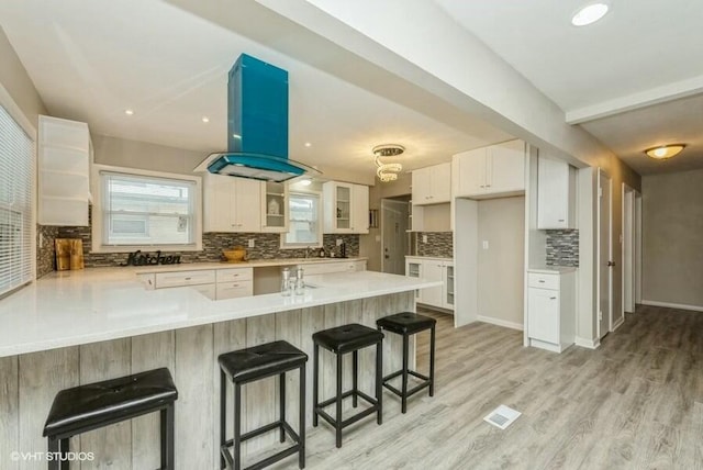 kitchen with white cabinets, kitchen peninsula, island exhaust hood, and light hardwood / wood-style flooring