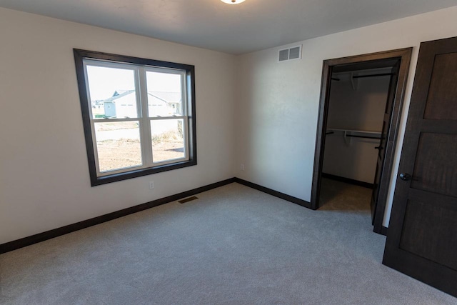 unfurnished bedroom with a spacious closet, light carpet, and a closet