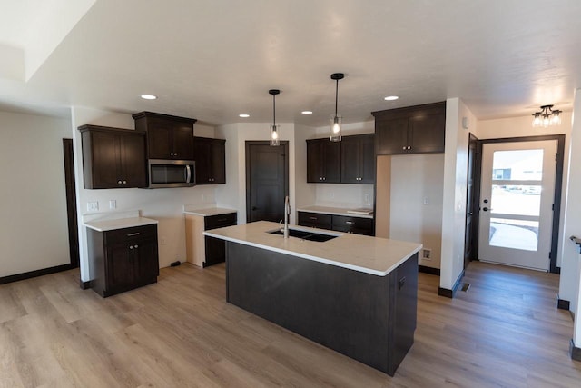 kitchen featuring a kitchen island with sink, hanging light fixtures, sink, light wood-type flooring, and dark brown cabinets