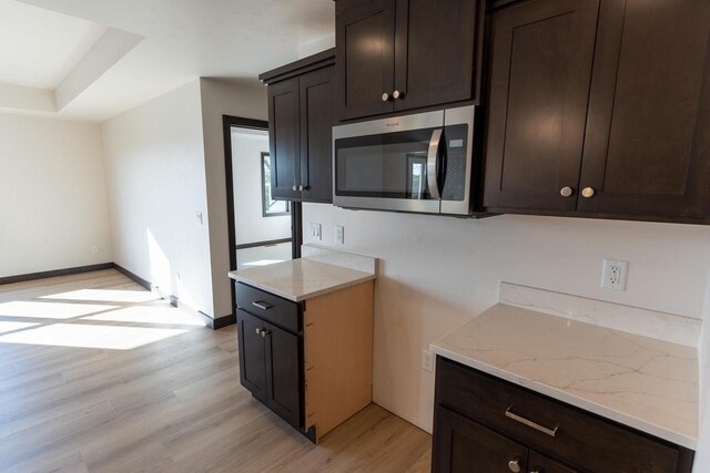 kitchen with dark brown cabinets, light wood-type flooring, and light stone counters