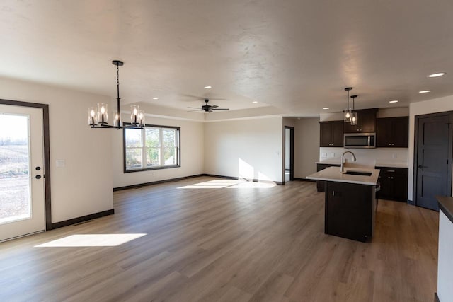 kitchen with pendant lighting, a center island with sink, ceiling fan with notable chandelier, sink, and dark brown cabinetry