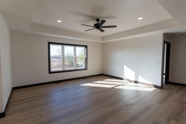 unfurnished room with hardwood / wood-style flooring, ceiling fan, and a tray ceiling