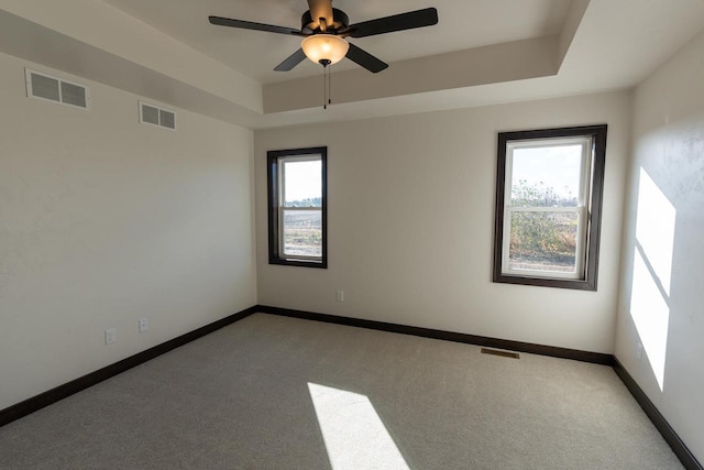 unfurnished room featuring a raised ceiling, ceiling fan, and light carpet