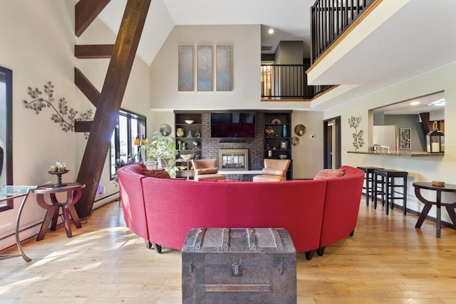 living room with a brick fireplace, baseboard heating, light hardwood / wood-style flooring, high vaulted ceiling, and beamed ceiling