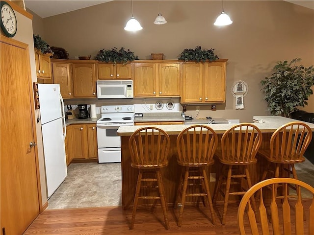 kitchen featuring light hardwood / wood-style flooring, pendant lighting, vaulted ceiling, white appliances, and a breakfast bar area