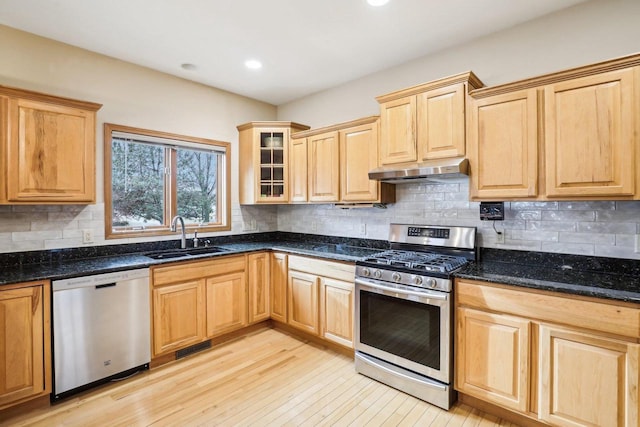 kitchen with appliances with stainless steel finishes, light hardwood / wood-style floors, sink, and dark stone countertops