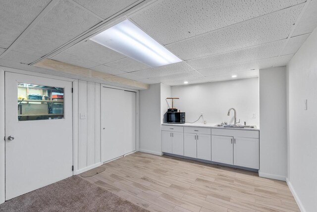 bar featuring white cabinets, a drop ceiling, light hardwood / wood-style floors, and sink