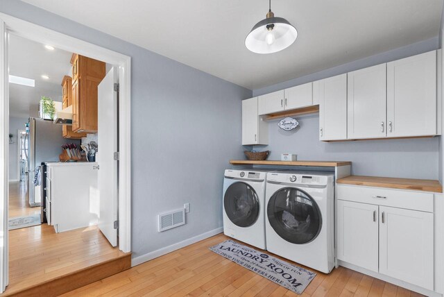 washroom with washing machine and dryer, cabinets, and light hardwood / wood-style floors