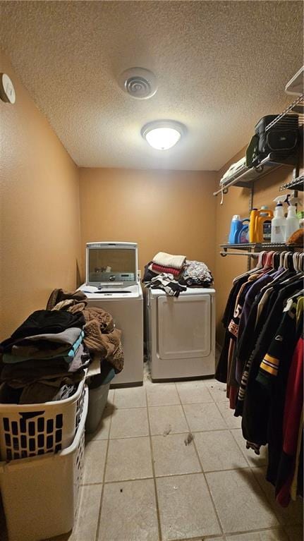 clothes washing area with a textured ceiling, washing machine and clothes dryer, and light tile patterned floors