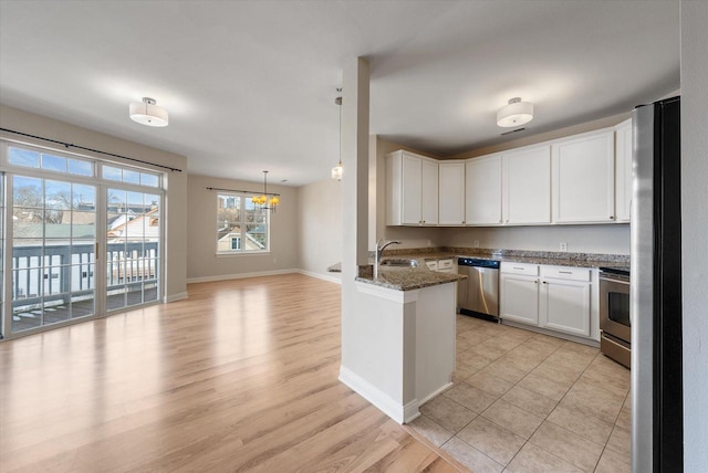 kitchen with white cabinetry, sink, kitchen peninsula, dark stone counters, and appliances with stainless steel finishes