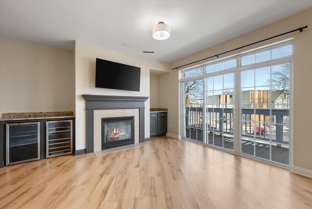 unfurnished living room with a fireplace, beverage cooler, and light hardwood / wood-style flooring