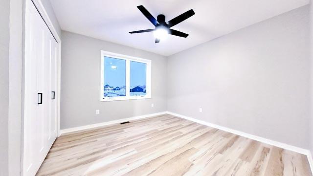 unfurnished bedroom with light wood finished floors, ceiling fan, baseboards, and a closet