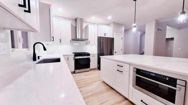 kitchen with a sink, freestanding refrigerator, wall chimney range hood, stainless steel oven, and stove