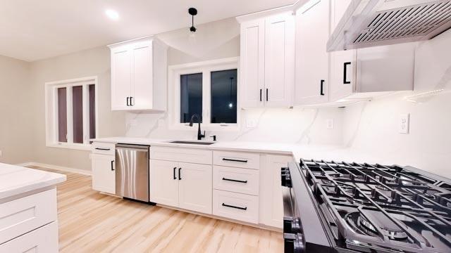 kitchen with a sink, stainless steel dishwasher, gas range oven, white cabinetry, and extractor fan