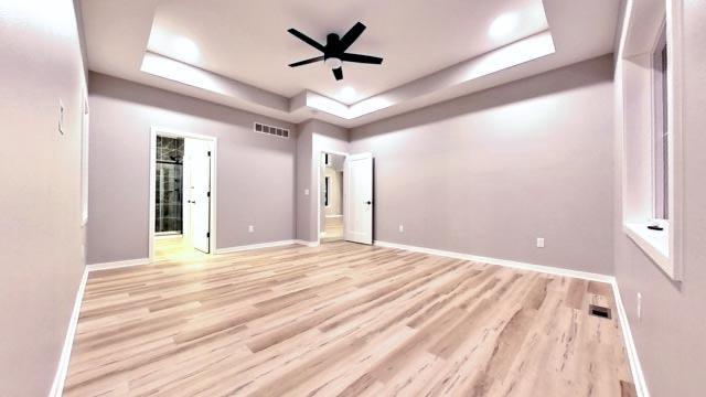 unfurnished room with light wood finished floors, visible vents, baseboards, a tray ceiling, and a ceiling fan