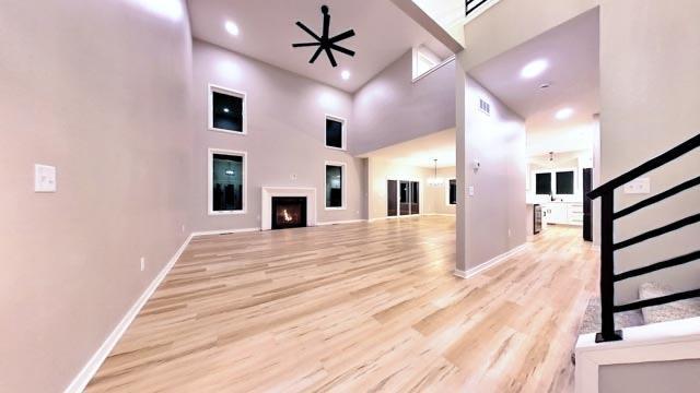 unfurnished living room with ceiling fan, light hardwood / wood-style floors, and a high ceiling