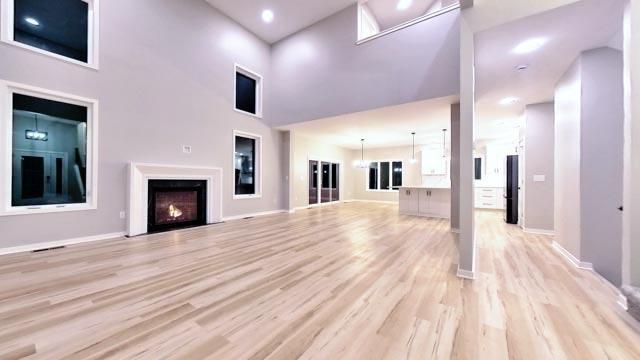 unfurnished living room featuring light wood-style floors, baseboards, a lit fireplace, and a high ceiling